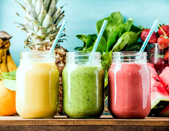 Freshly blended fruit smoothies of various colors and tastes in glass jars. Yellow, red, green. Turquoise blue background